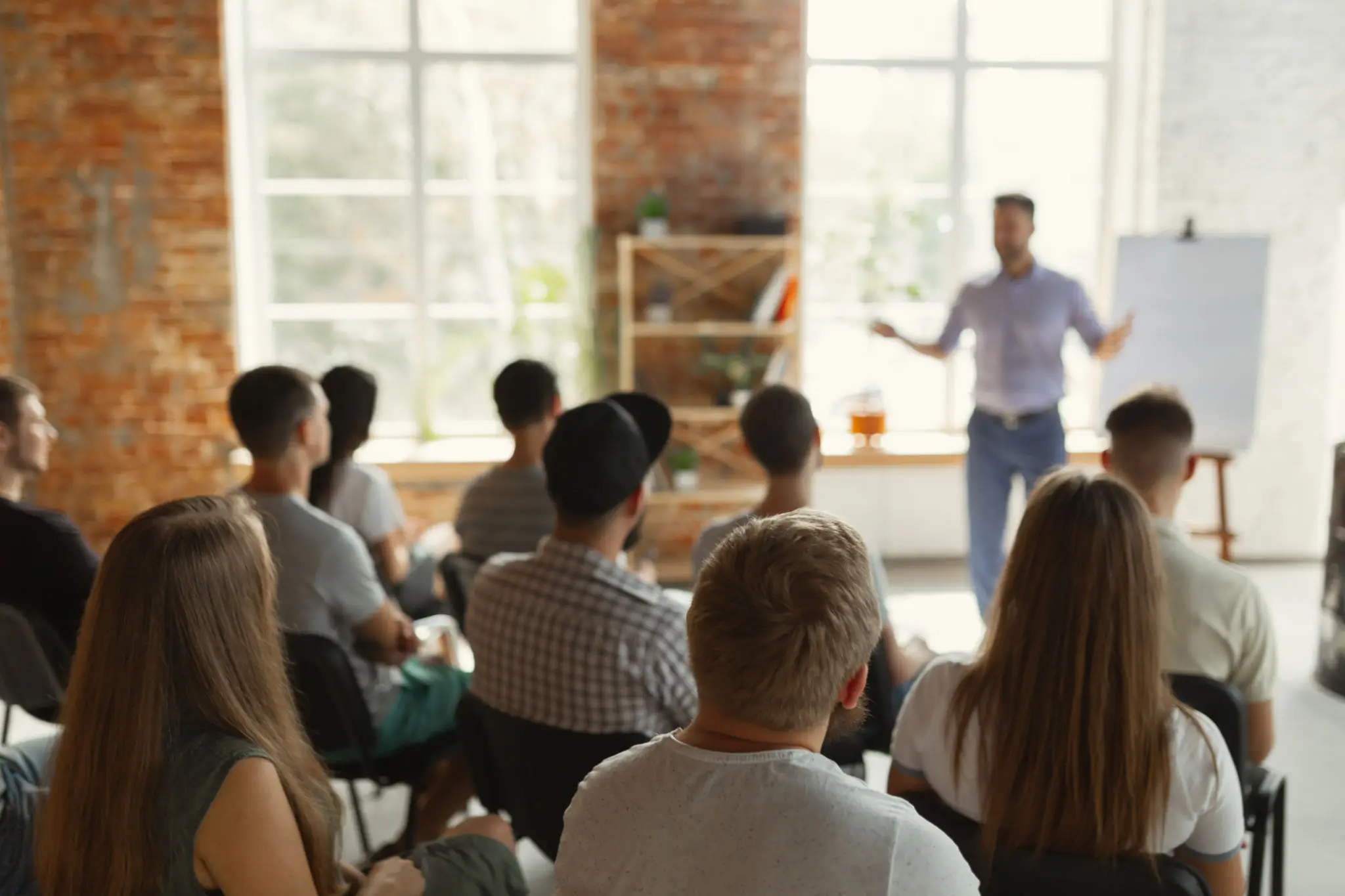 Speaker addressing a seated audience in a bright room.